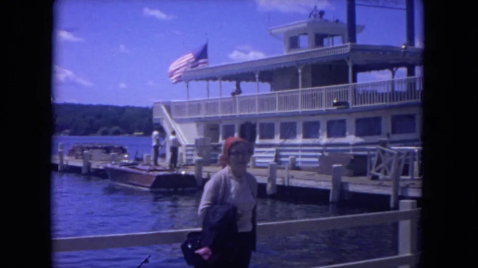 1972 riverfront footage shows a woman near the dock rail as passengers and a large white boat appear behind her.