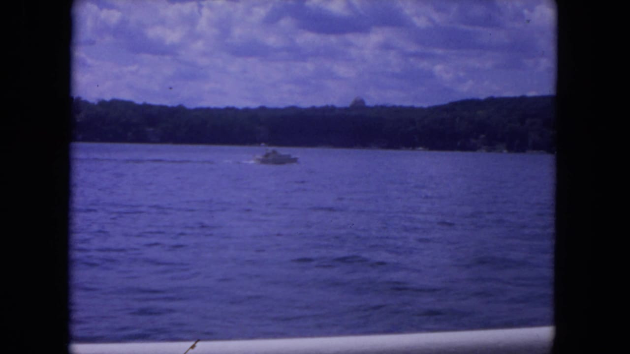 Late-frame 1972 Mississippi River view with a speedboat, rippled water, wooded horizon, and aged purple-blue 8mm color.