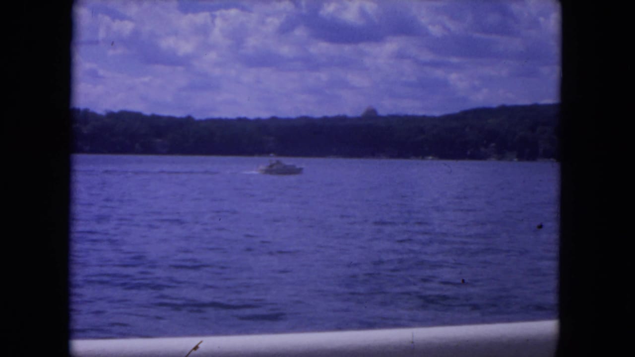 Open water with a small motorboat under a cloudy sky and dark film-frame edges.