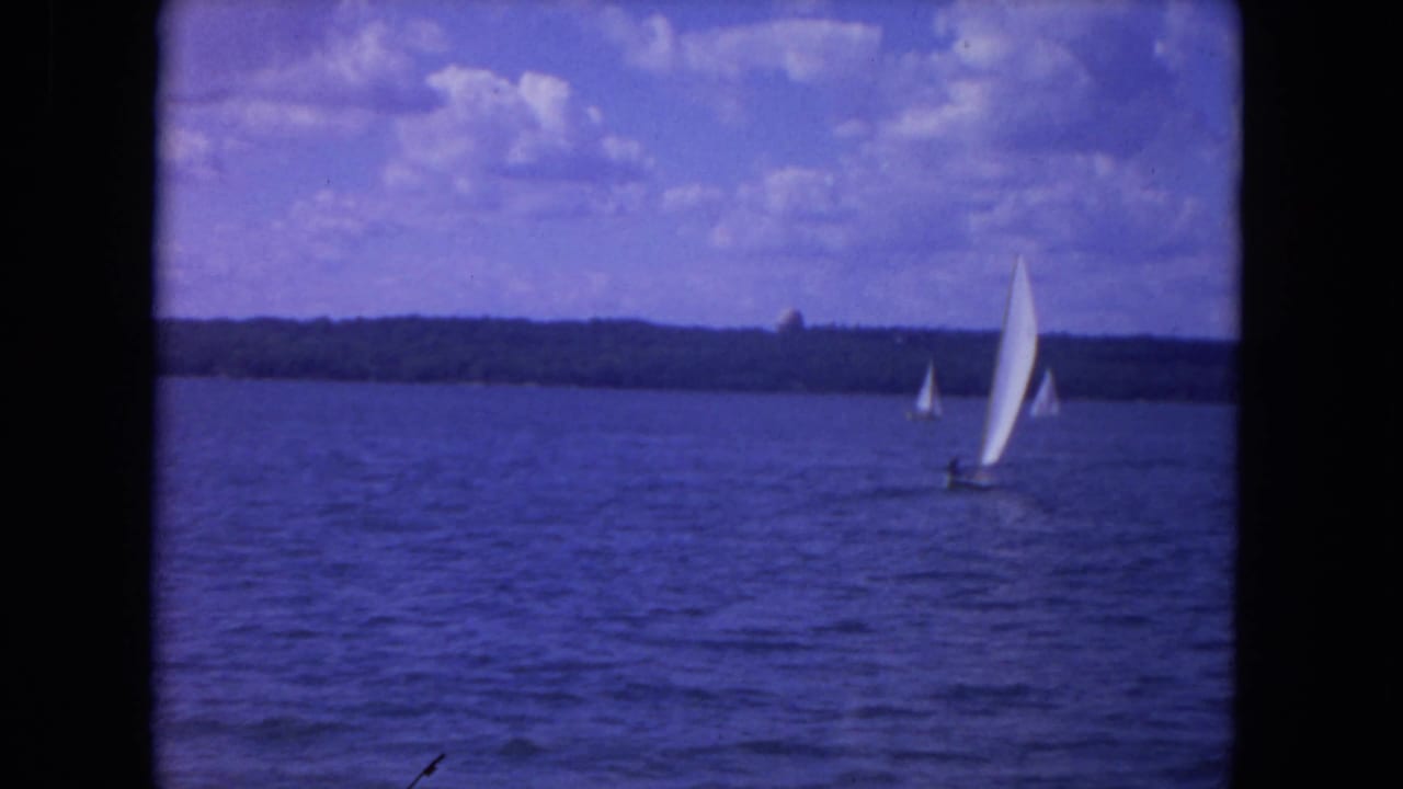 White sailboats on blue river water beneath a partly cloudy sky.