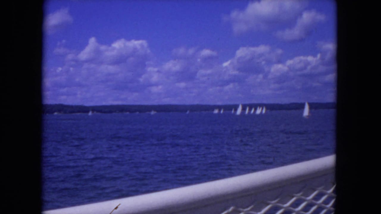 Sailboats on blue river water under a cloudy sky, viewed past a boat railing.