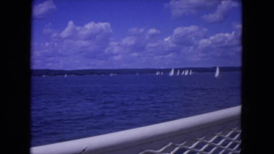 1972 Mississippi River sailing scene with clustered white sails, dark shoreline, and foreground boat rail.
