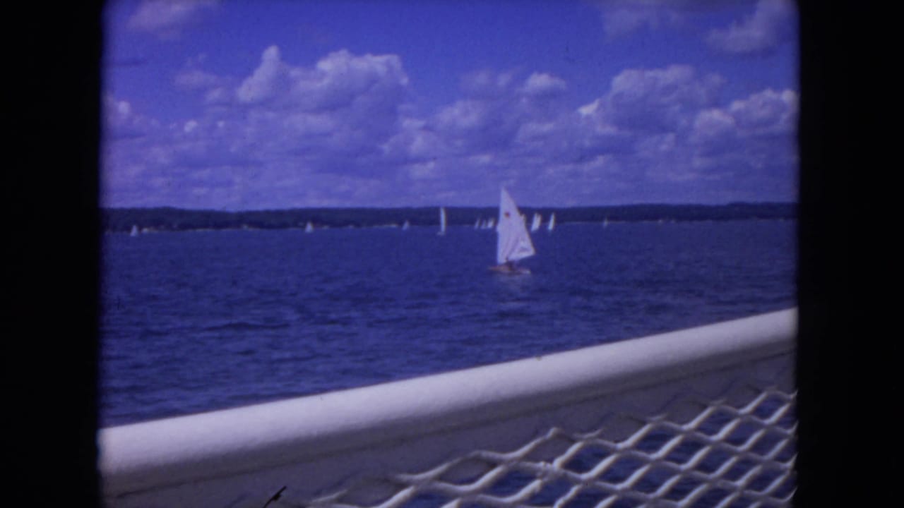 Sailboats on blue river water beyond a white railing and mesh foreground.