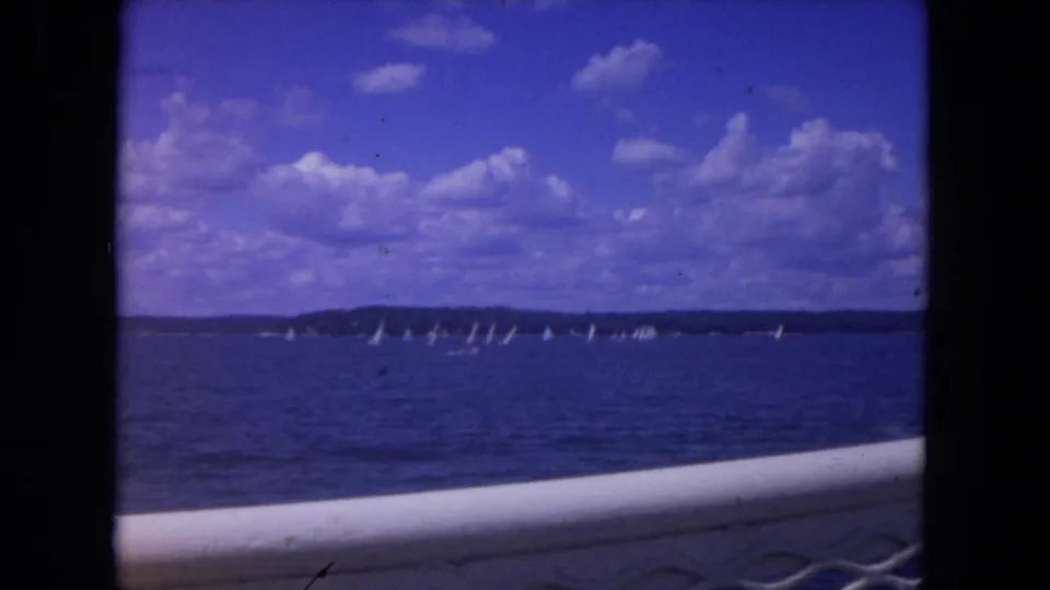1972 8mm view from a boat on the Mississippi River, with distant sailboats across blue water under a partly cloudy sky.