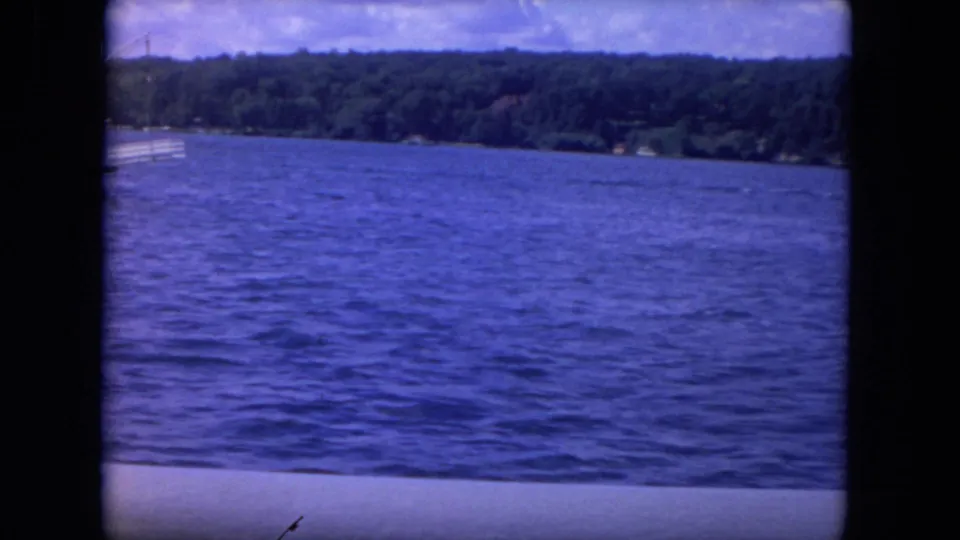 1972 8mm Mississippi River frame with the riverboat almost out of view, emphasizing open water, distant trees, and cloudy sky.