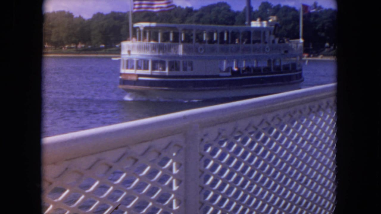White riverboat with an American flag passing behind a lattice railing on blue water.