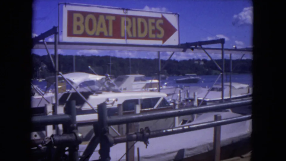 The final 8mm frame holds on the BOAT RIDES sign and nearby marina boats, confirming a recreational river dock setting.