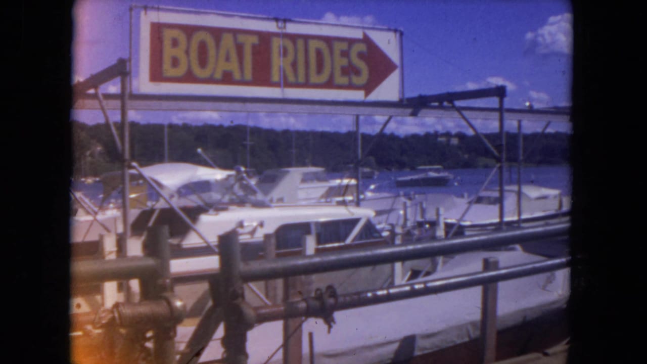 BOAT RIDES sign above docked white motorboats at a small marina.