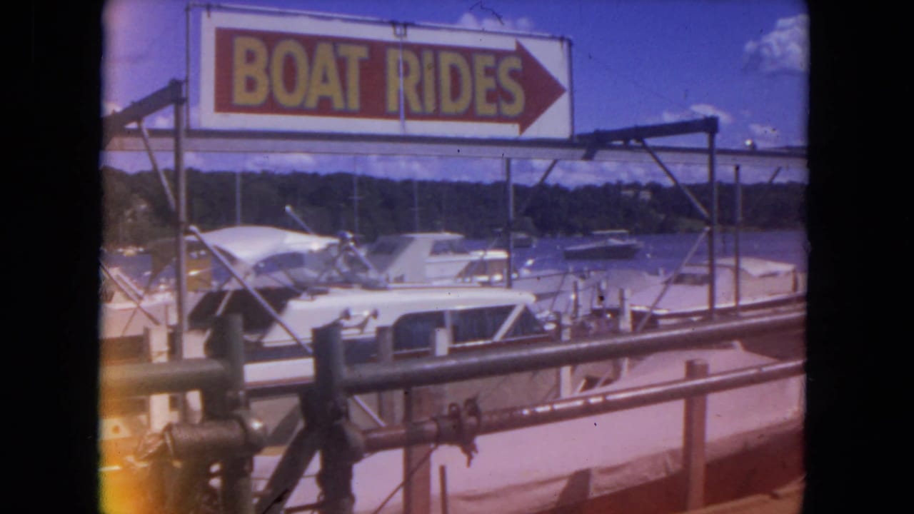 Boat rides sign and docked boats seen through 8mm frame edges.