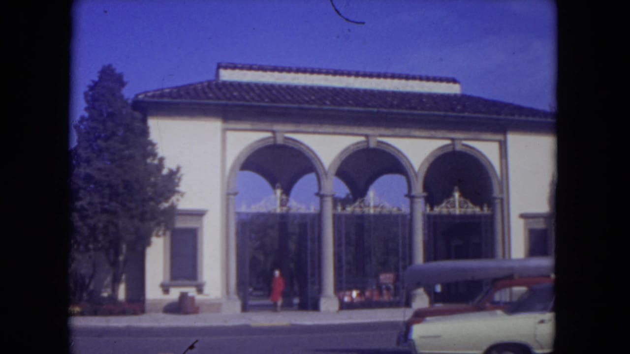 Woman in red coat near an arched building entrance with a parked car at the curb.