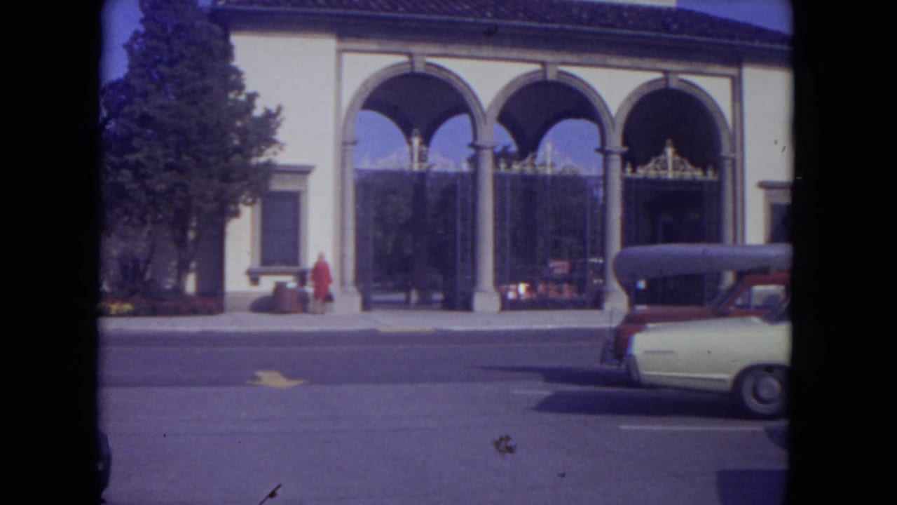 Arched building facade with a woman in red and a car partly visible at right.
