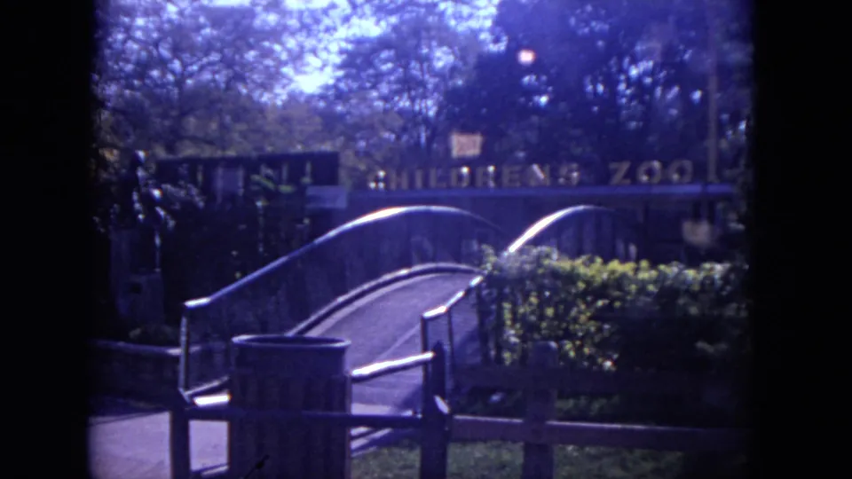 Lincoln Park Zoo visitor area with a small bridge, shrubs, trash can, and partially visible Children's Zoo sign in 1972 footage.