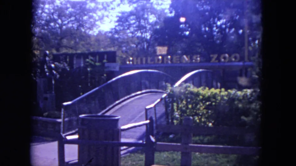 1972 8mm view of the Children's Zoo entrance area at Lincoln Park Zoo, with a curved bridge, railings, trees, and signage.