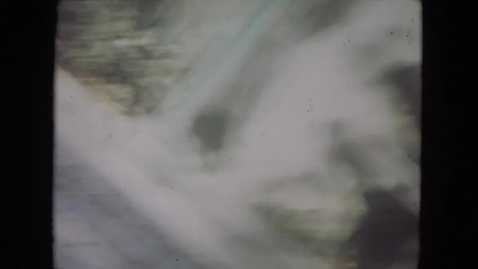 Blurred 8mm frame from the supplied 1972 Lincoln Park zoo clip, showing a pale outdoor enclosure area and dark film edges.