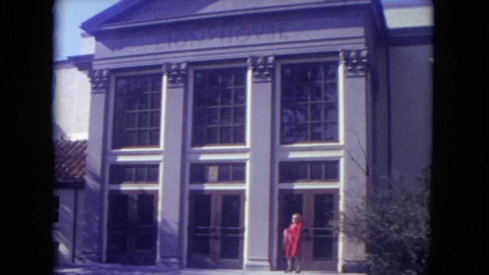 Lincoln Park zoo building facade from the supplied 1972 clip, with tall windows, columns, and a woman in a red coat at the doorway.