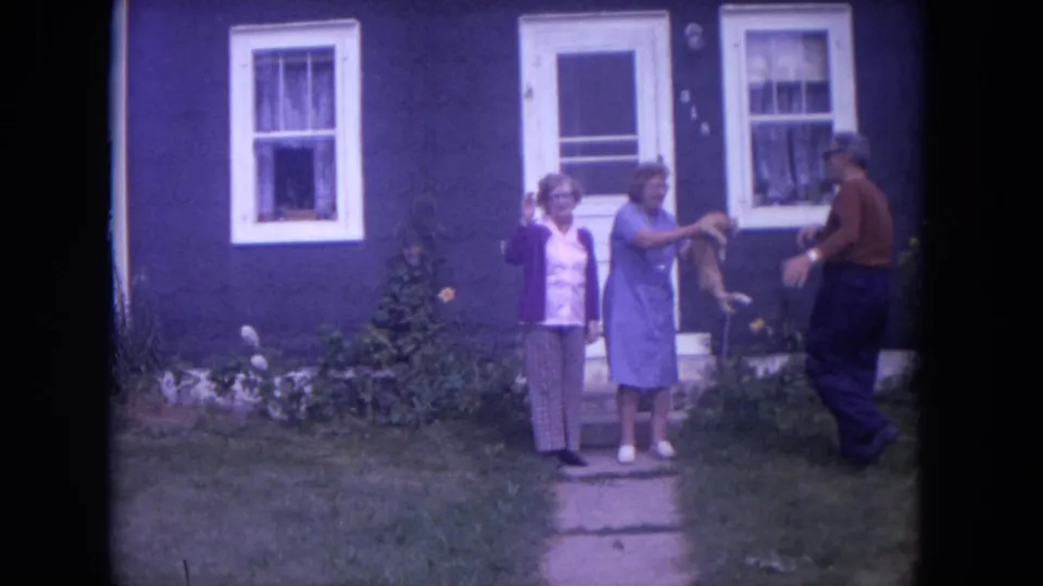 A man approaches two women outside a Lake Geneva house as the woman in blue holds out a cat.