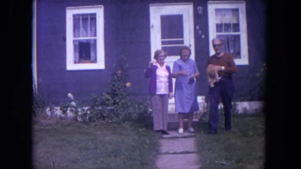 The man stands holding the cat next to two women on a lawn in front of the Lake Geneva house.