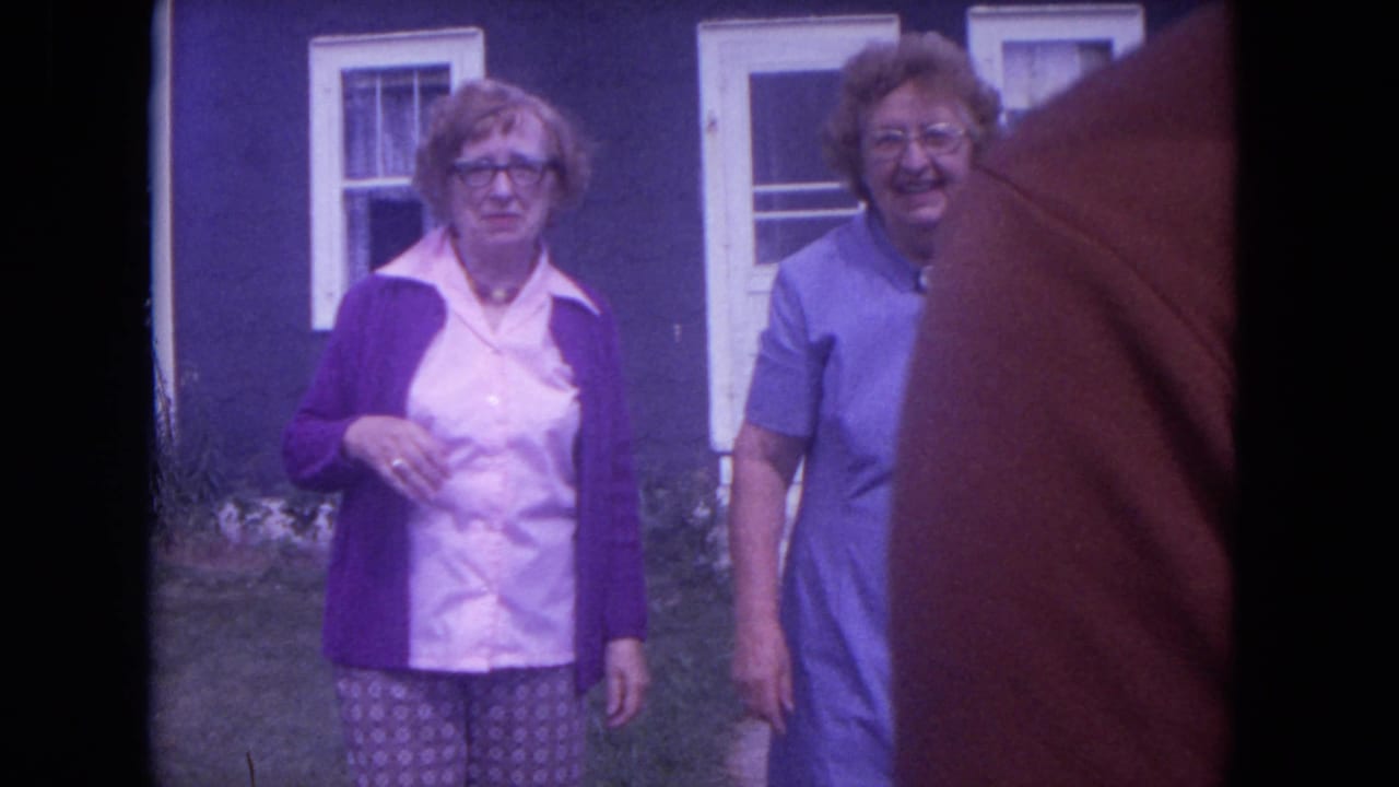 In Lake Geneva, Wisconsin in 1972, two women stand near a purple-sided house while an orange cat partially obscures the 8mm frame.