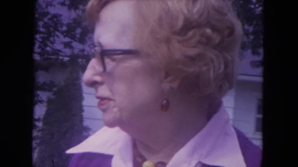Older woman in glasses and a purple outfit seen in side profile outdoors in Lake Geneva, Wisconsin, in 1972 home-movie footage.