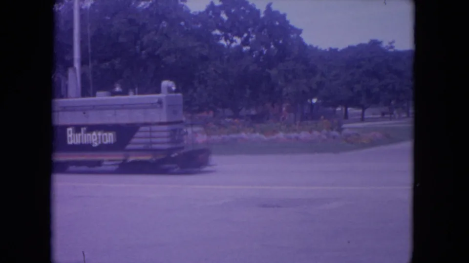 A small train marked Burlington moves through a tree-lined Lake Geneva park area in 1972 8mm home-movie footage.