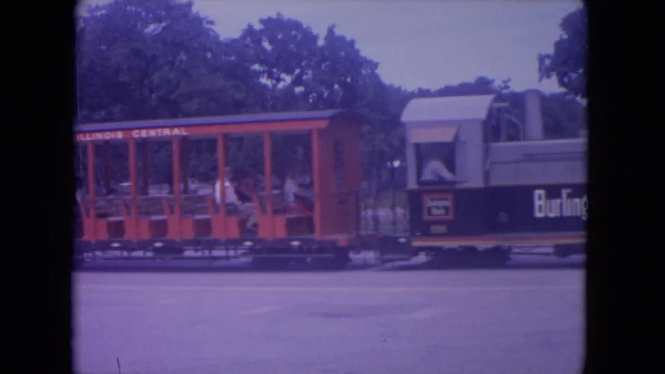 1972 Colby, Wisconsin 8mm frame showing a red Illinois Central open-air park train car beside a small locomotive body.
