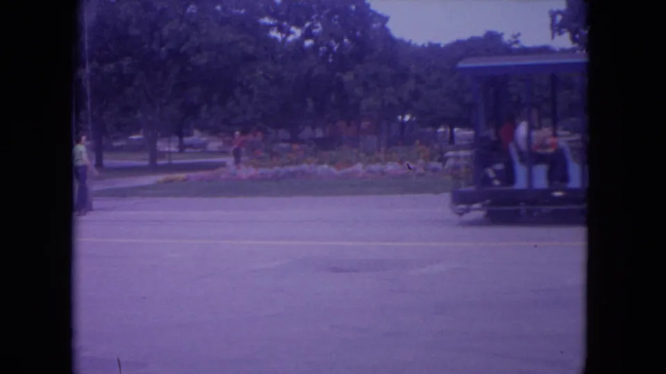 The children's train exits the frame in a 1972 Colby, Wisconsin home-movie shot, with landscaping and a few people visible nearby.