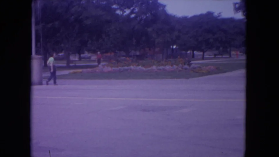 1972 Colby, Wisconsin home-movie frame showing distant visitors beside a road, trees, and planted grounds near the zoo setting.