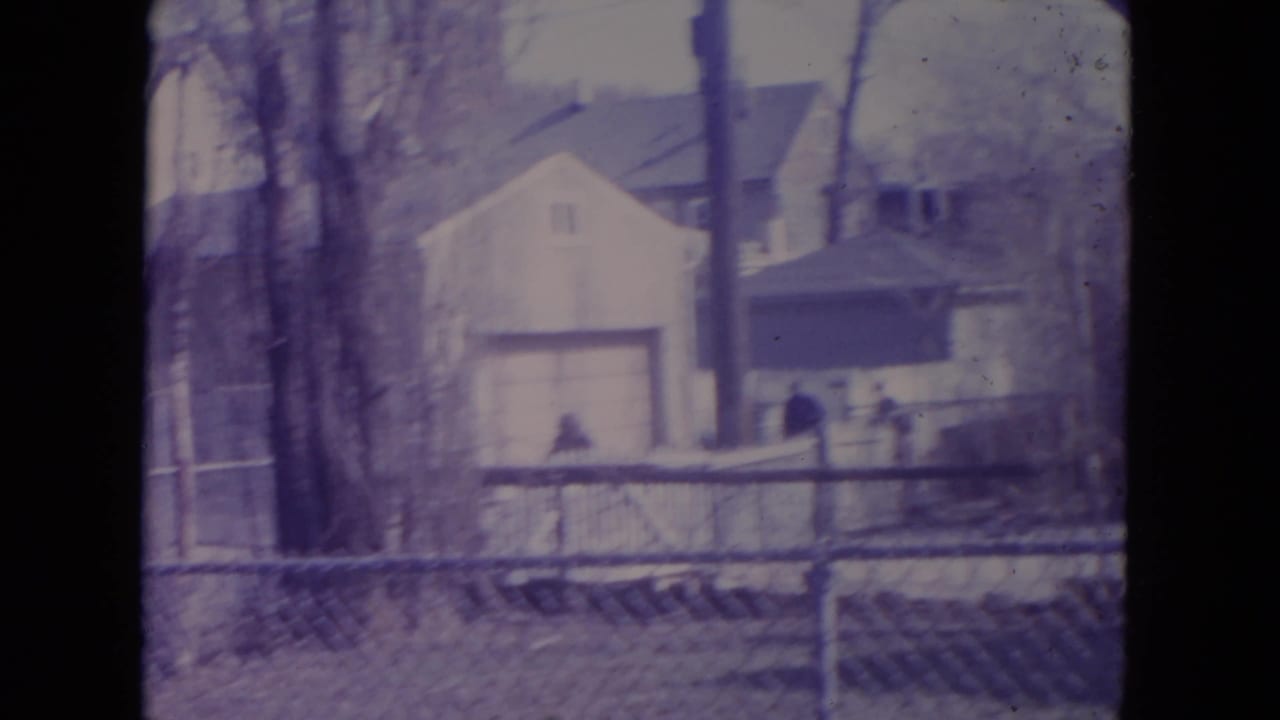 A fenced Racine residential yard with a house and garage in the background and distant people near the fence.