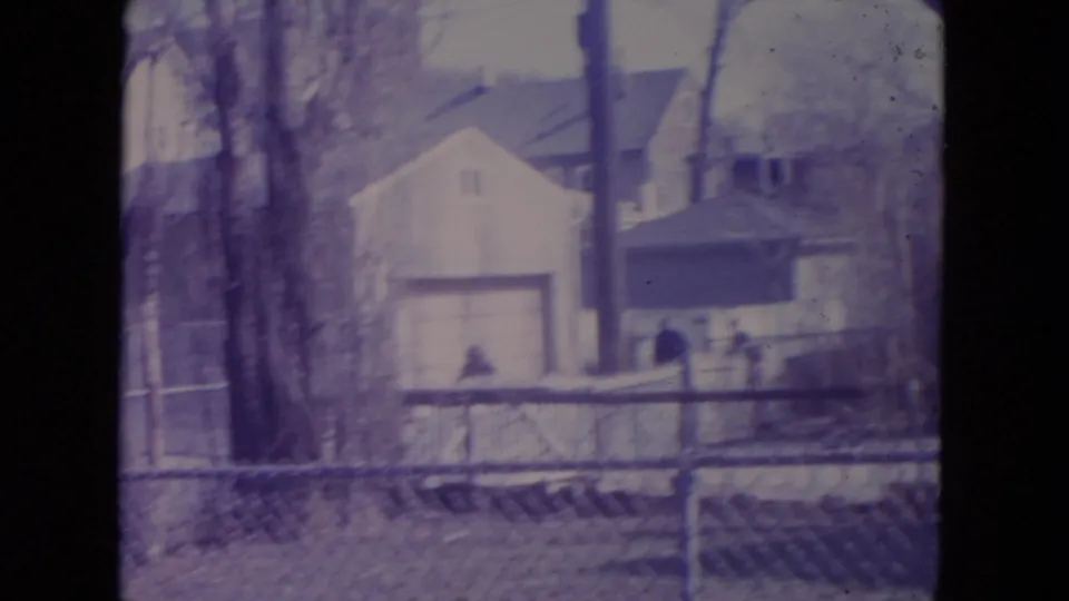 A fenced Racine residential yard with a house and garage in the background and distant people near the fence.