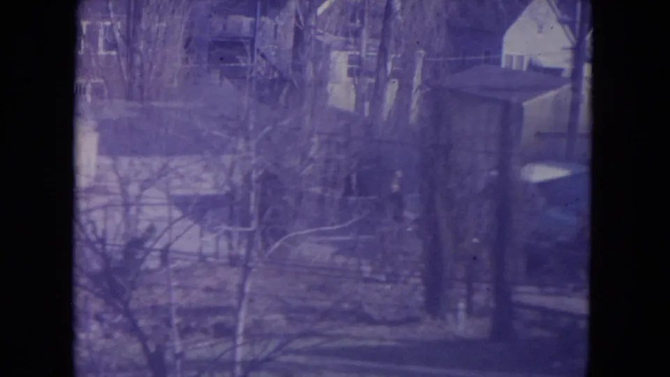 Purple-shifted 8mm frame of a leafless residential yard in Racine, Wisconsin, with houses, trees, and a parked car visible.