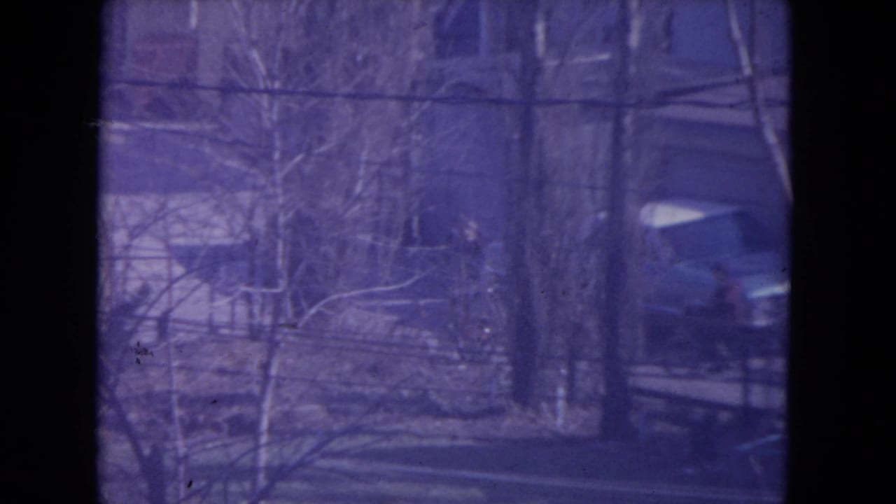 Racine 1972 home-movie frame showing bare trees, a residential yard, a house, and a car with visible 8mm grain.