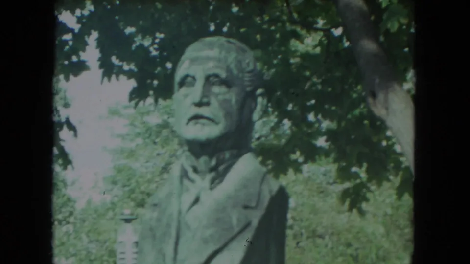 A weathered stone bust appears in a leafy Racine, Wisconsin park setting, seen in soft 1972 home-movie footage.