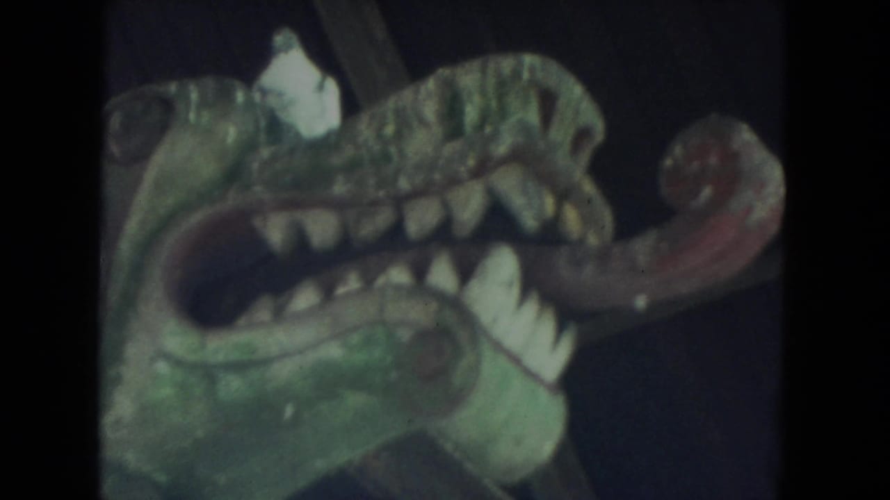 Painted creature head with open mouth, teeth, and red tongue.