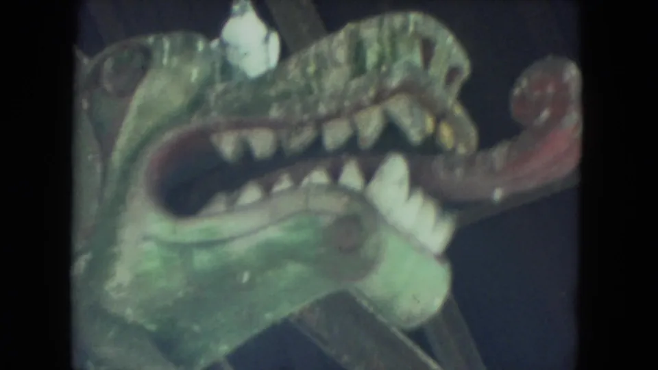 Handheld 8mm close-up of the same painted creature head, showing its open mouth, teeth, tongue, and worn surface.
