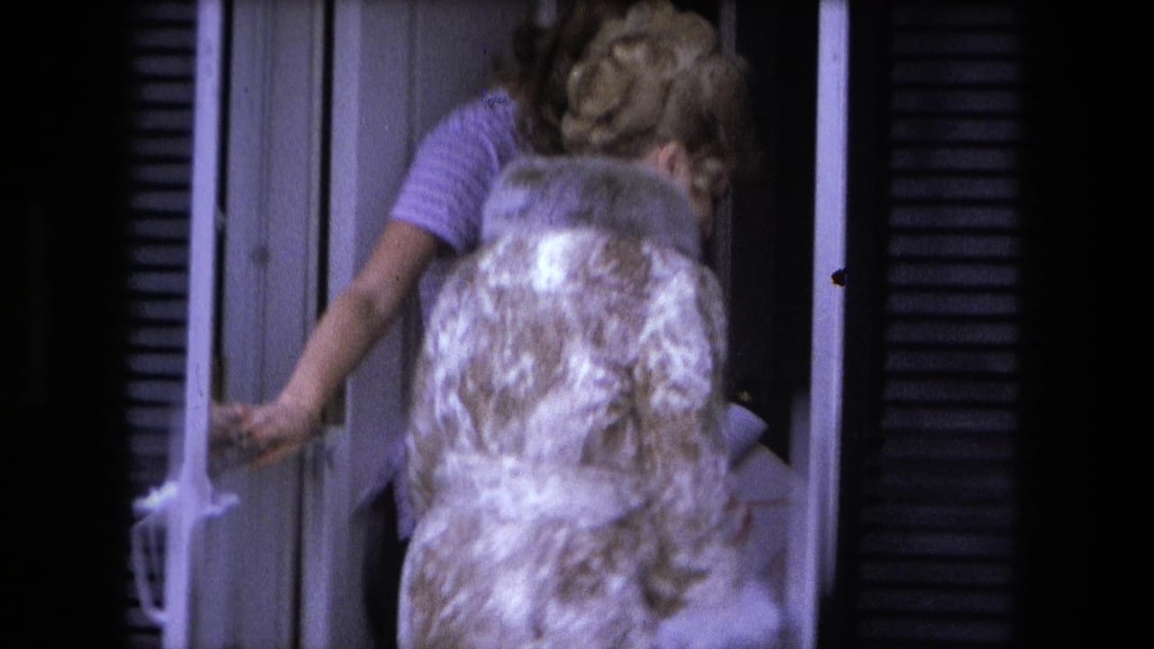 In Fort Wayne home-movie footage from 1973, a woman in a patterned coat exits while another woman stands in the doorway of a suburban house.