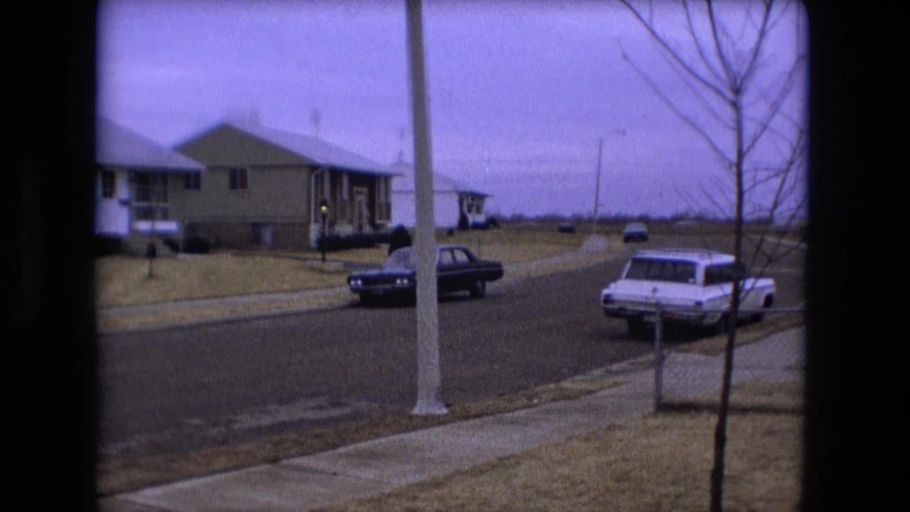 1973 Fort Wayne neighborhood street with ranch-style houses, a white station wagon, a dark sedan, bare trees, and overcast sky.