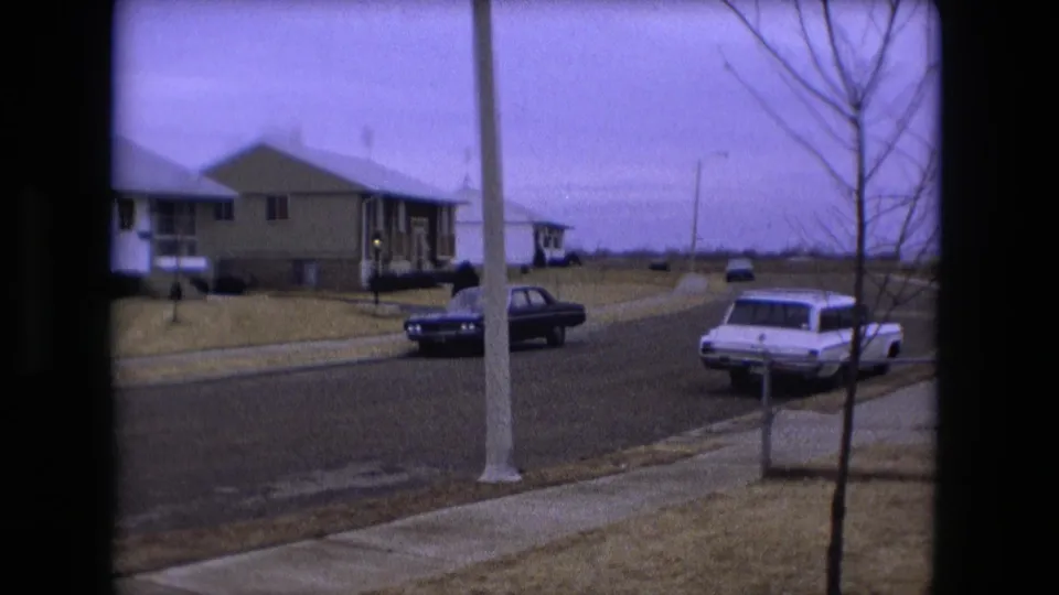 1973 Fort Wayne neighborhood street with ranch-style houses, a white station wagon, a dark sedan, bare trees, and overcast sky.