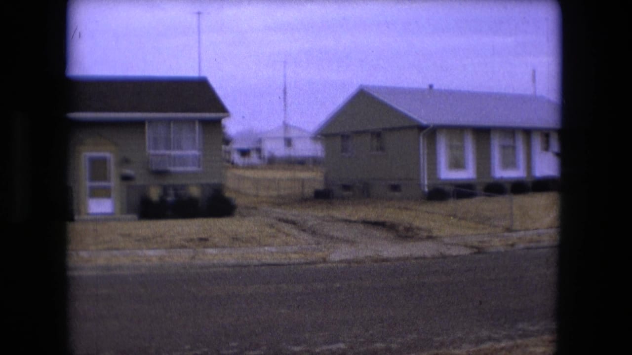 1973 Fort Wayne home-movie frame showing green suburban houses, a dry lawn, curb, and quiet residential street.
