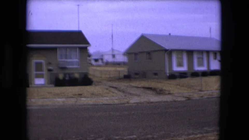 1973 Fort Wayne home-movie frame showing green suburban houses, a dry lawn, curb, and quiet residential street.