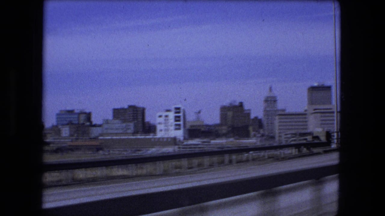 Fort Wayne skyline appears beyond the roadway and guardrail during a moving 8mm vehicle shot from 1973.