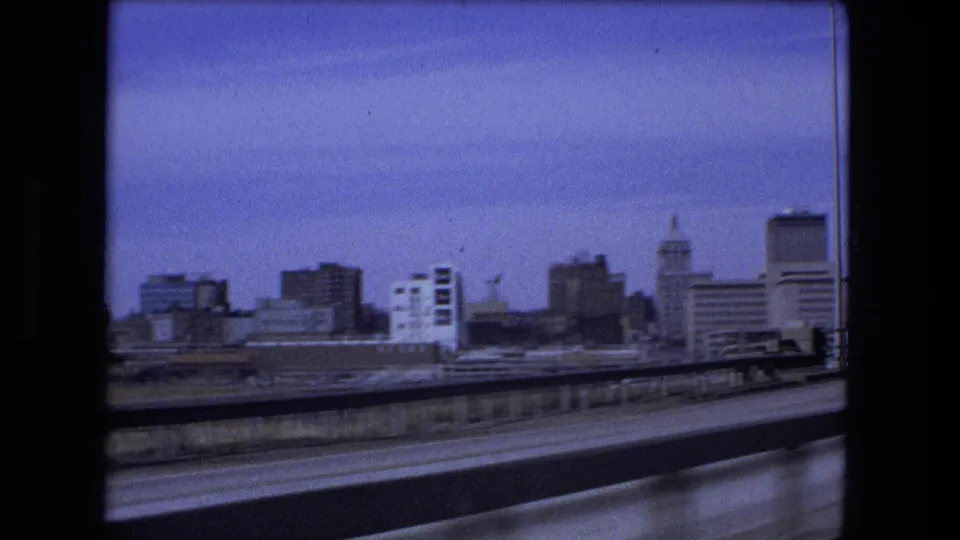 Fort Wayne skyline appears beyond the roadway and guardrail during a moving 8mm vehicle shot from 1973.