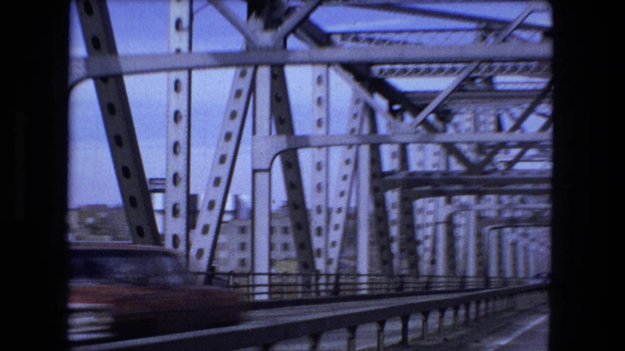 Steel bridge structure seen from a moving vehicle with a blurred car passing at left.
