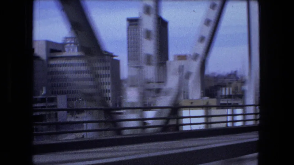 Fort Wayne city buildings appear through the bridge structure, with vertical steel beams and roadside railings framing the downtown view.