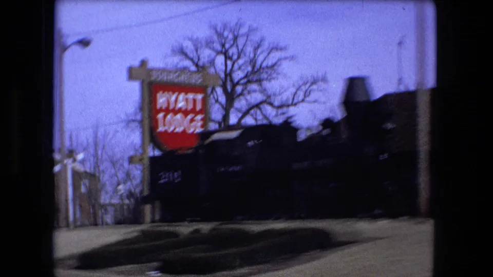 Roadside view in the Fort Wayne sequence with a red Hyatt Lodge sign, bare tree branches, and dark building frontage.