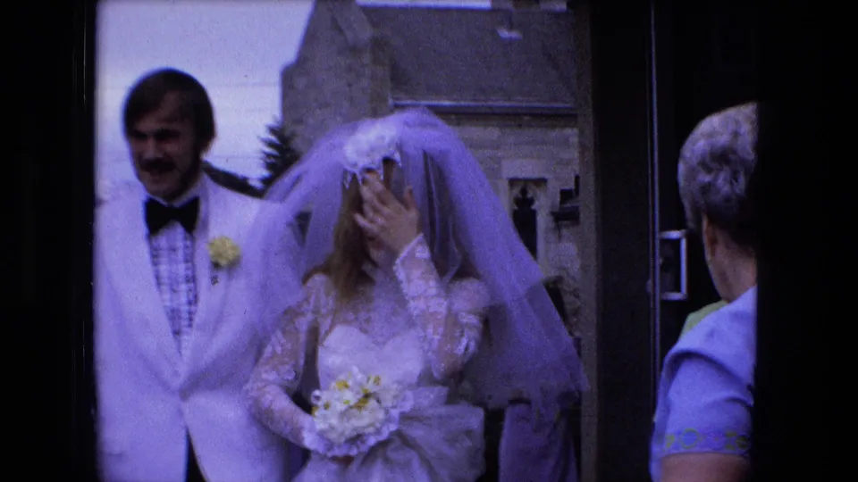 1973 Fort Wayne wedding footage showing a groom in a white jacket beside a veiled bride holding a bouquet outside a church entrance.