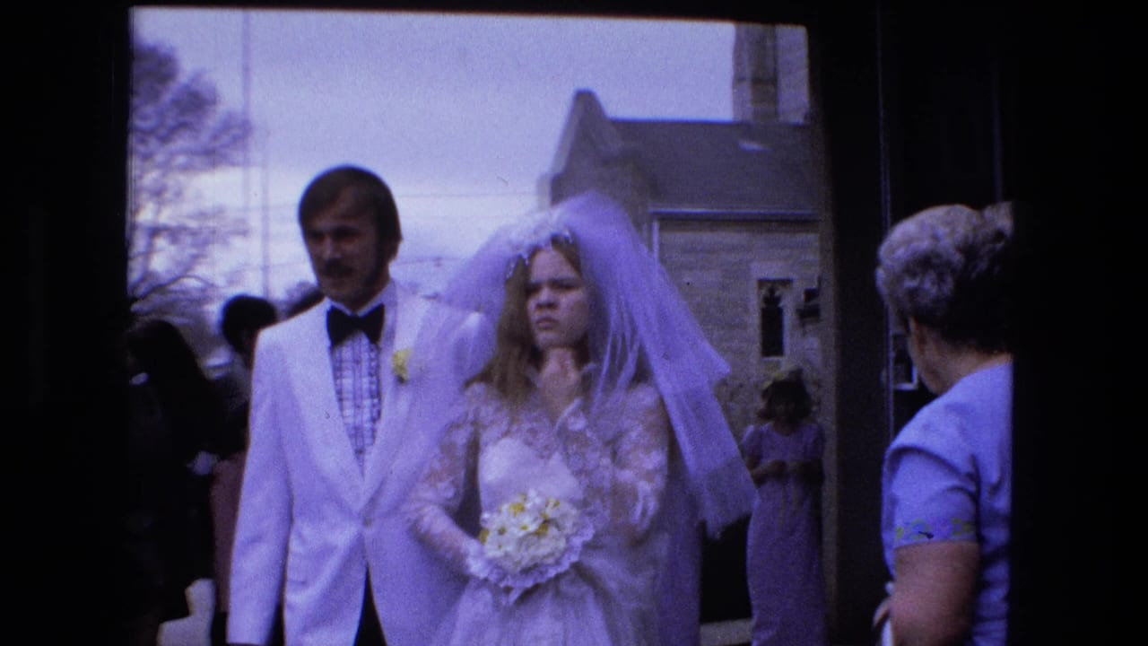 Bride and groom walk outdoors through wedding guests beside a building.