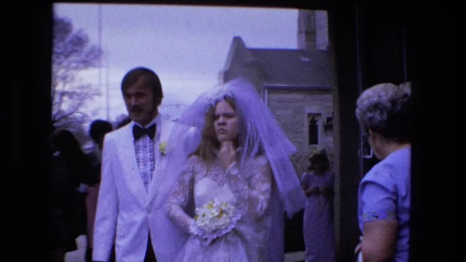 In Fort Wayne, Indiana, a bride in a veil and groom in a white tuxedo walk past guests after a 1973 wedding.