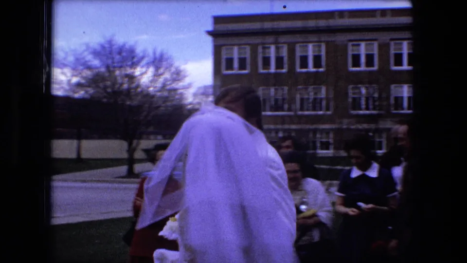In Fort Wayne, Indiana, a 1973 bride and groom walk toward seated wedding guests outside near a brick building.