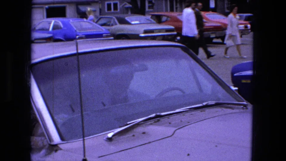 The bride and groom continue down the street behind the foreground windshield of a parked car in Fort Wayne.
