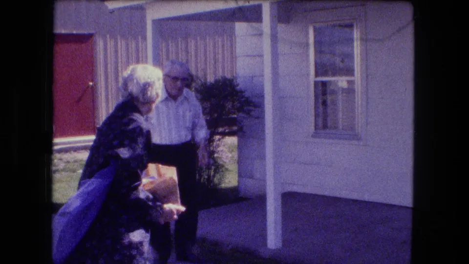 The 1973 Fort Wayne porch scene shows an older woman carrying a bag beside an older man, with a red door and curtained window behind them.